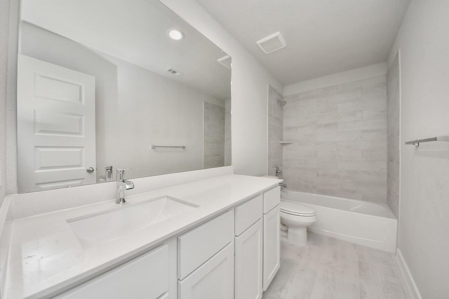 Secondary bath features tile flooring, bath/shower combo with tile surround, light stained wood cabinets, beautiful light countertop. Sample photo of completed home with similar floor plan. Actual colors and selections may vary.