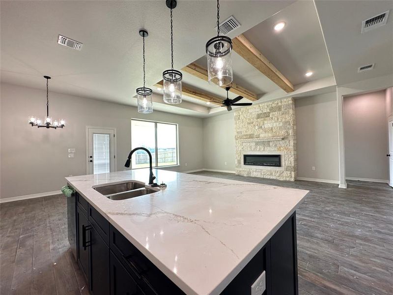 Kitchen featuring dark cabinets, beamed ceiling, dark wood finished floors, pendant lighting, and light stone counters Kitchen featuring dark cabinets, beamed ceiling, dark wood finished floors, pendant lighting, and light stone counters
