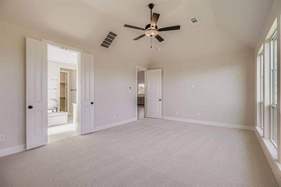 Unfurnished bedroom featuring lofted ceiling, light carpet, a ceiling fan, and ensuite bathroom
