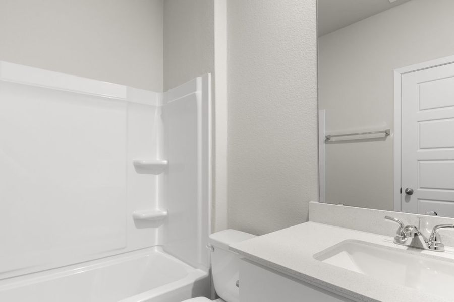 Image of a bathroom with a white vinyl bathroom, a white vanity with white cabinets and a large mirror