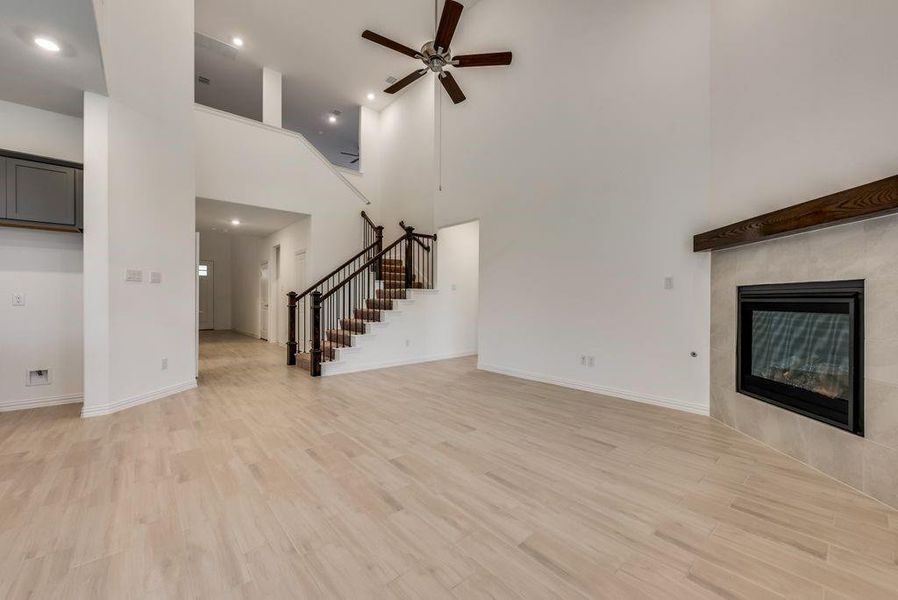 Unfurnished living room with a fireplace, a towering ceiling, ceiling fan, and light hardwood / wood-style flooring