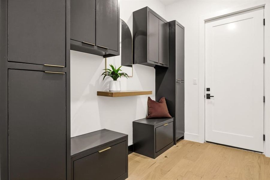 Built-in mudroom cabinetry featuring dark flat-panel doors, gold-tone hardware, and a light wood-finish flooring