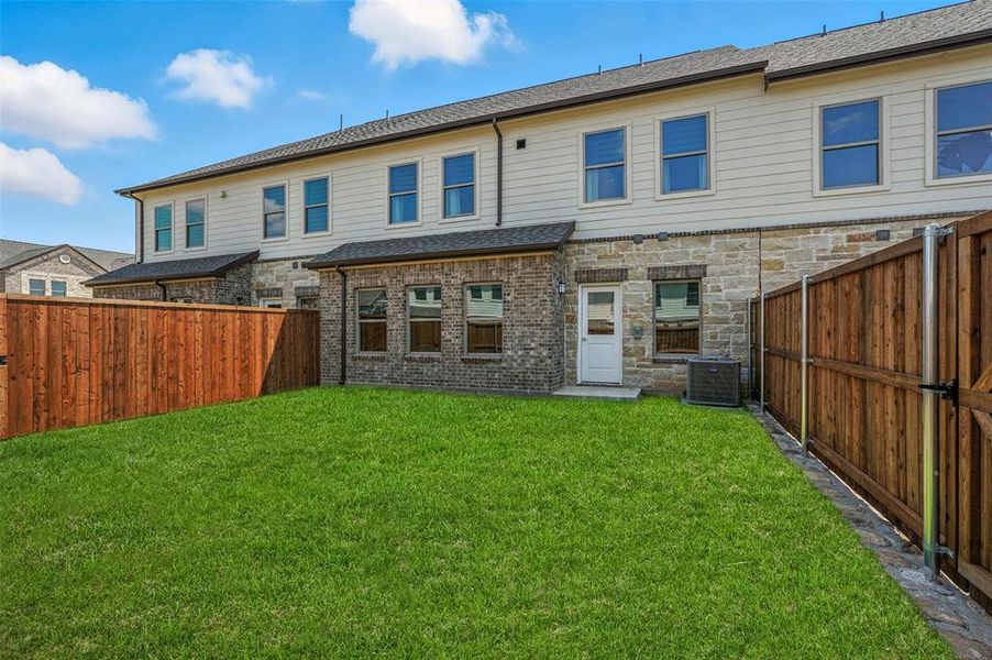 Back of house featuring a fenced backyard, a shingled roof, and stone siding