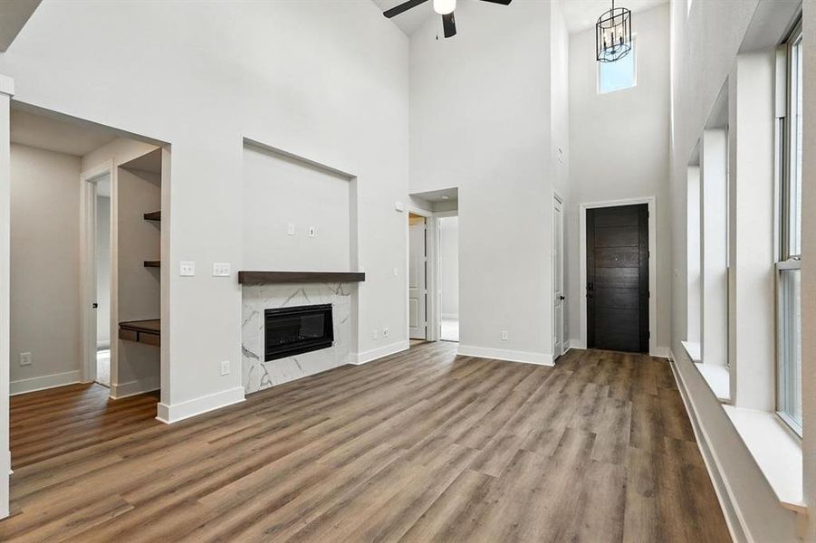 Unfurnished living room with wood finished floors, a high ceiling, a high end fireplace, and ceiling fan Unfurnished living room with wood finished floors, a high ceiling, a high end fireplace, and ceiling fan
