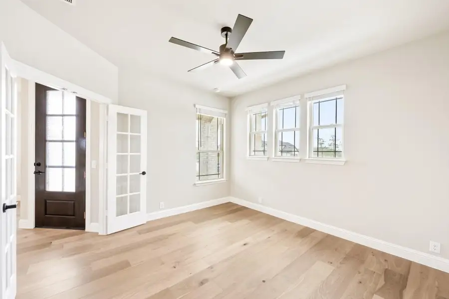 Empty room with light hardwood floors, ceiling fan, French doors, and multiple windows
