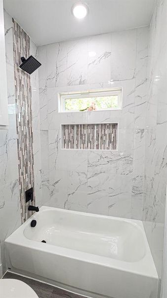 Hallway bathroom with tiled shower / bath combo, toilet, and plenty of natural light