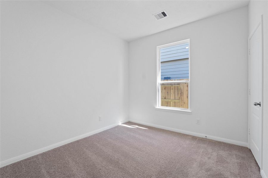 This secondary bedroom offers comfort and style with plush carpeting, neutral paint tones, recessed lighting, a large window with blinds, and a walk-in closet.
