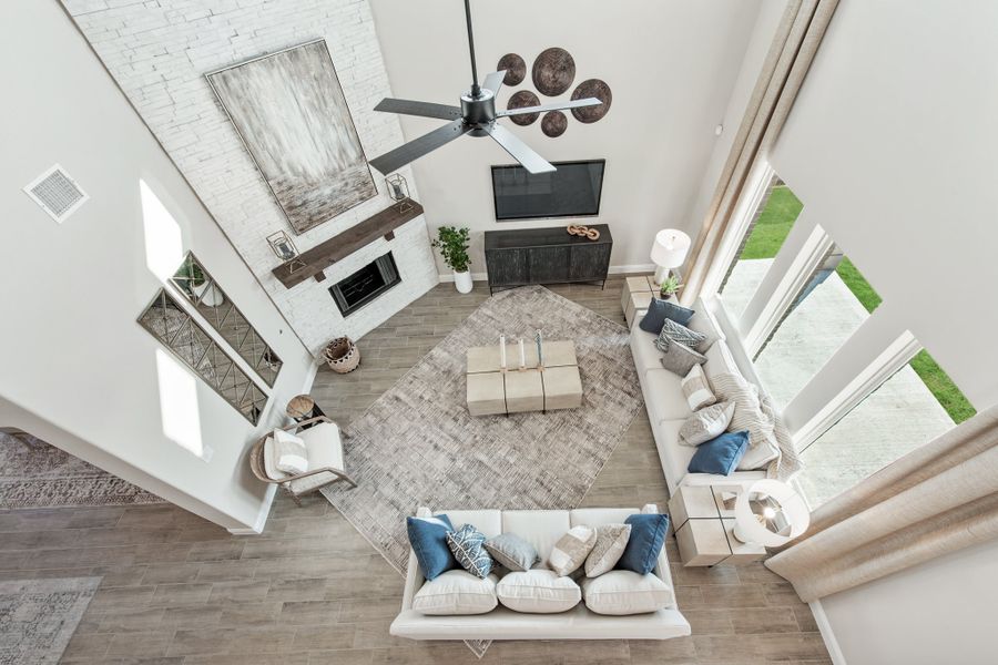 Overhead view of open living room with high ceilings, white brick fireplace, sectional sofa, and large windows Overhead view of open living room with high ceilings, white brick fireplace, sectional sofa, and large windows