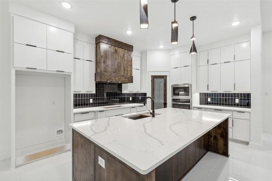 Kitchen featuring stainless steel appliances, sink, decorative light fixtures, and an island with sink