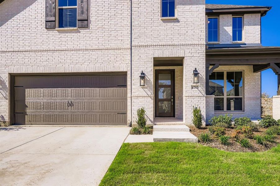 Property entrance with brick siding, driveway, covered porch, a garage, and a lawn