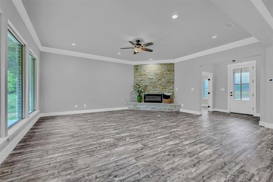 Unfurnished living room featuring wood-type flooring, ceiling fan, a fireplace, and crown molding