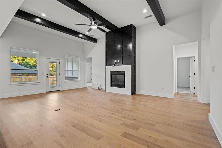 Unfurnished living room with beam ceiling, light wood-style flooring, a towering ceiling, a high end fireplace, and ceiling fan