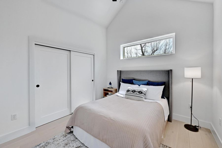 Bedroom with a closet, baseboards, high vaulted ceiling, and wood finished floors