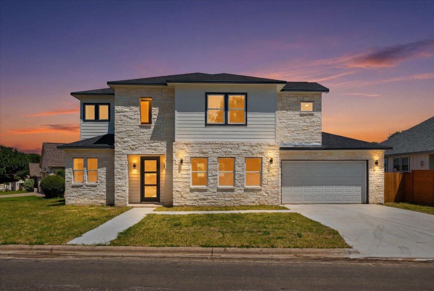 Stone and siding create an elegant, modern facade, with warm interior lighting glowing against a vibrant sunset.