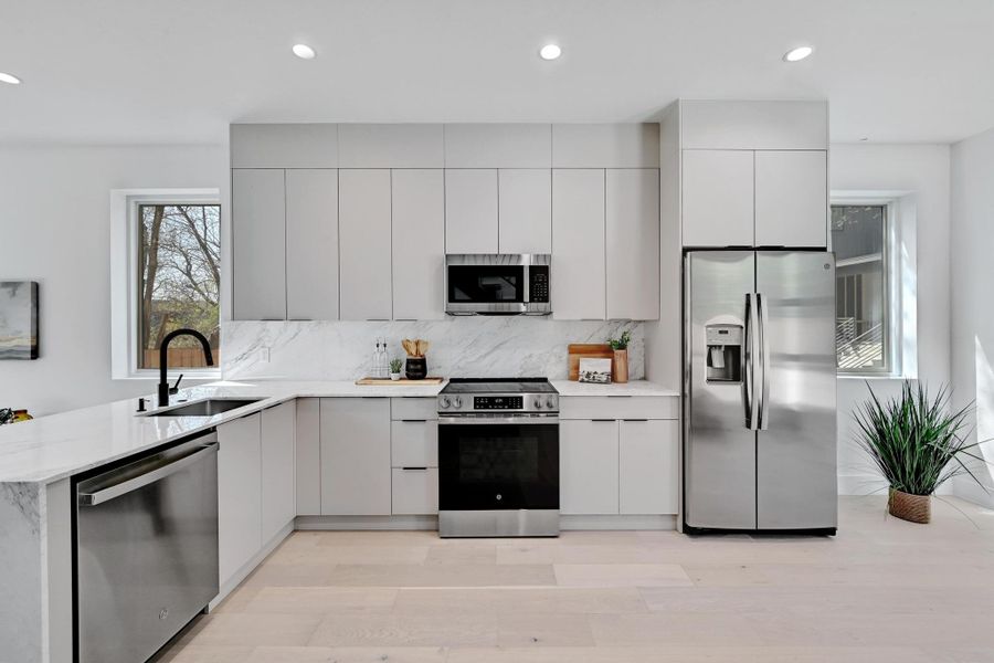 Kitchen with decorative backsplash, modern cabinets, appliances with stainless steel finishes, and a sink