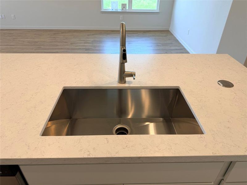 Kitchen island featuring a large undermount stainless steel sink, a modern brushed nickel faucet, and a light-toned countertop