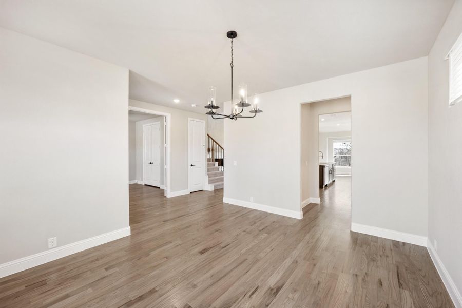 Empty dining room with dark hardwood floors, black chandelier, and open view to staircase and kitchen
