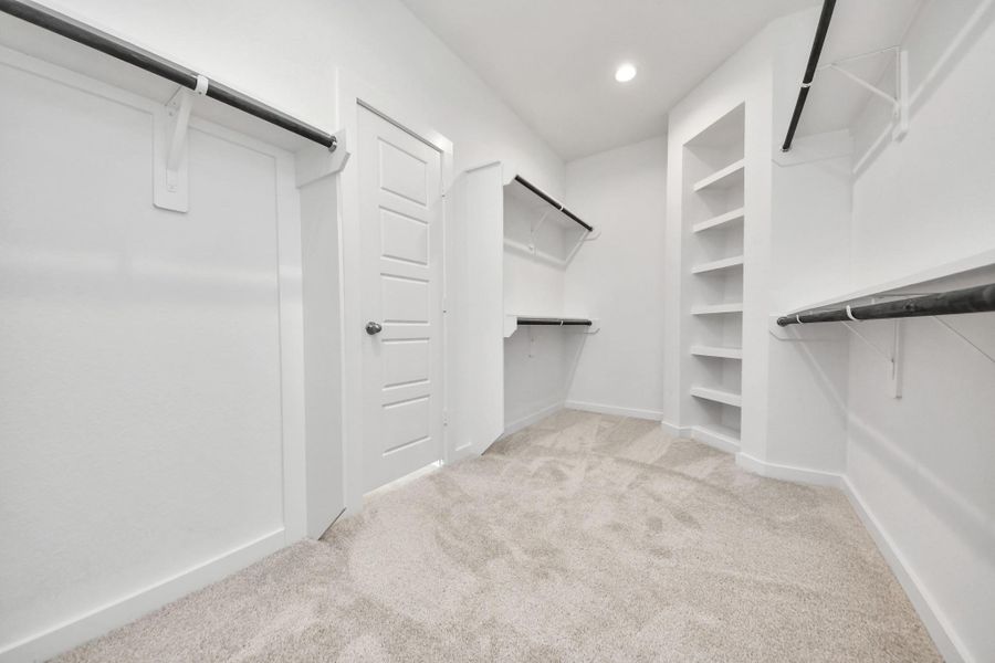 Walk-in closet that epitomizes luxury and practicality. This generously sized space features built-in shelving, offering abundant room for impeccable organization. High ceilings and recessed lighting create a bright and welcoming ambiance. Sample photo of completed home with similar floor plan. Actual colors and selections may vary.