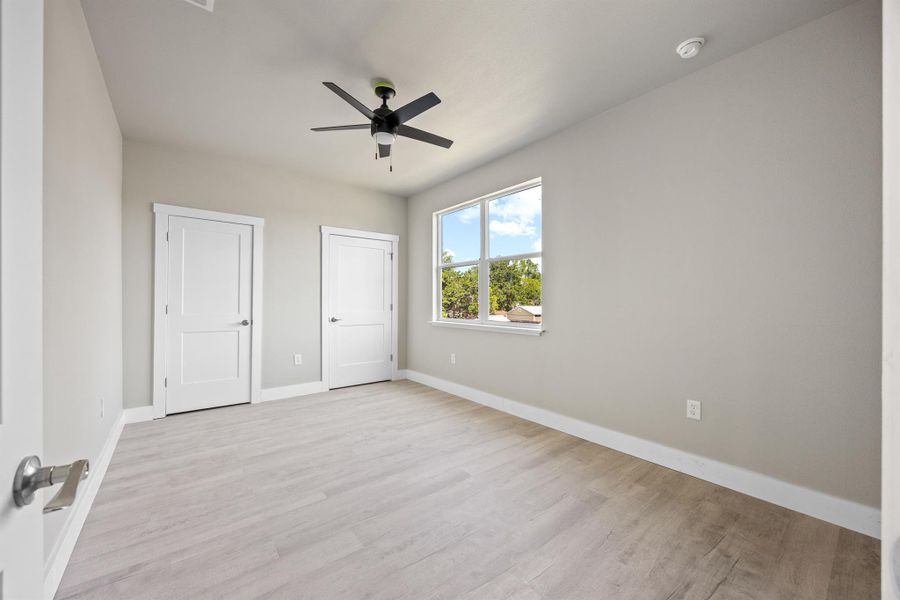 Unfurnished bedroom featuring multiple closets, light wood-style flooring, ceiling fan, and baseboards Unfurnished bedroom featuring multiple closets, light wood-style flooring, ceiling fan, and baseboards