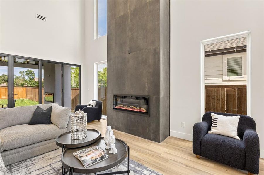 Expansive living area featuring a floor-to-ceiling fireplace with an integrated linear firebox, soaring ceilings, light wood-finish flooring, and large glass sliding doors providing abundant natural light