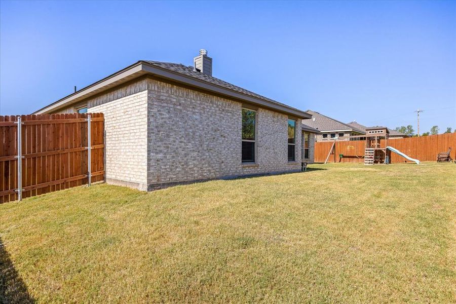 Rear view of property with a fenced backyard, brick siding, a chimney, and a playground