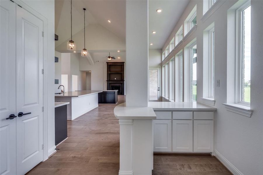 Kitchen with hanging light fixtures, white cabinets, hardwood / wood-style floors, black oven, and high vaulted ceiling