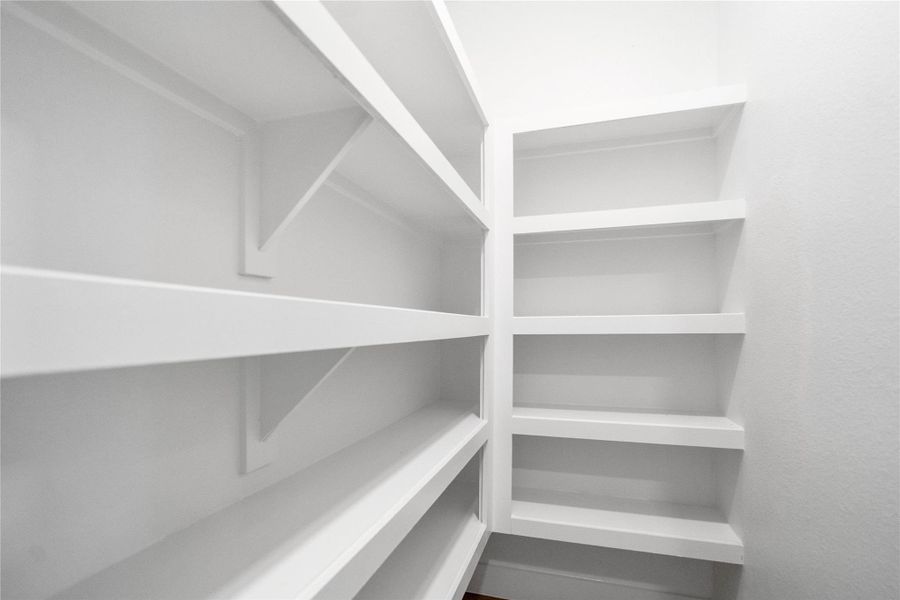 Spacious walk-in pantry offers exceptional storage potential, featuring multiple tiers of sturdy, built-in white shelving. Designed for maximum organization, the deep shelves provide ample space for all your culinary needs.