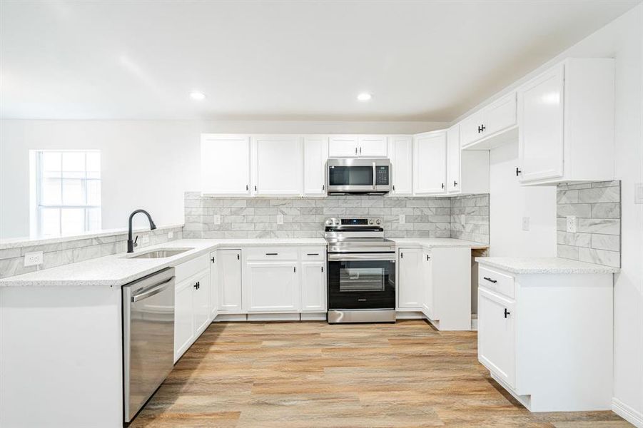 Kitchen with decorative backsplash, light hardwood / wood-style floors, appliances with stainless steel finishes, and sink