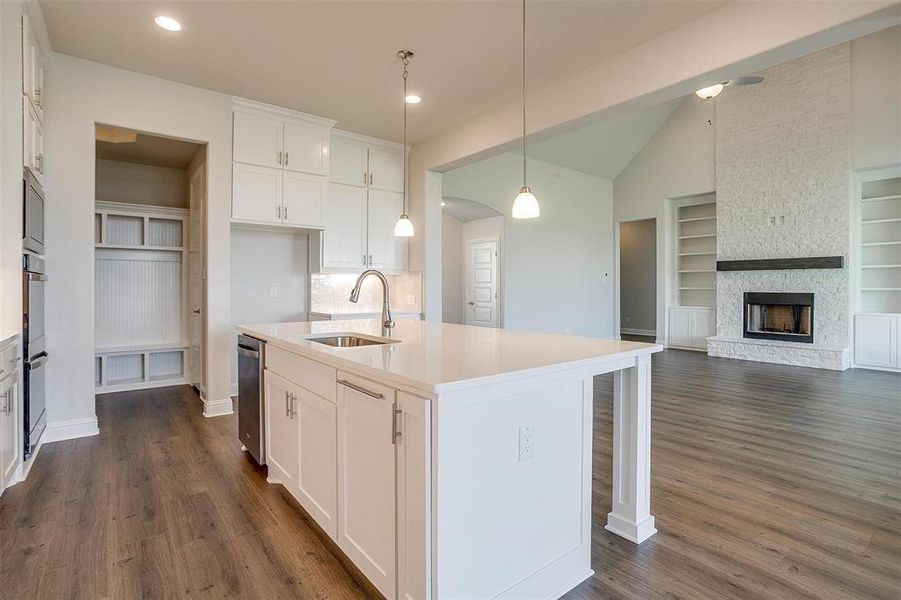 Kitchen with a kitchen island with sink, sink, white cabinets, built in shelves, and hanging light fixtures