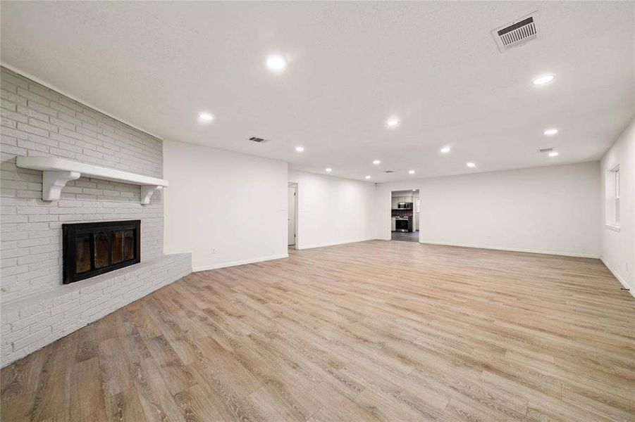 Unfurnished living room with light wood-type flooring, a brick fireplace, visible vents, and recessed lighting Unfurnished living room with light wood-type flooring, a brick fireplace, visible vents, and recessed lighting