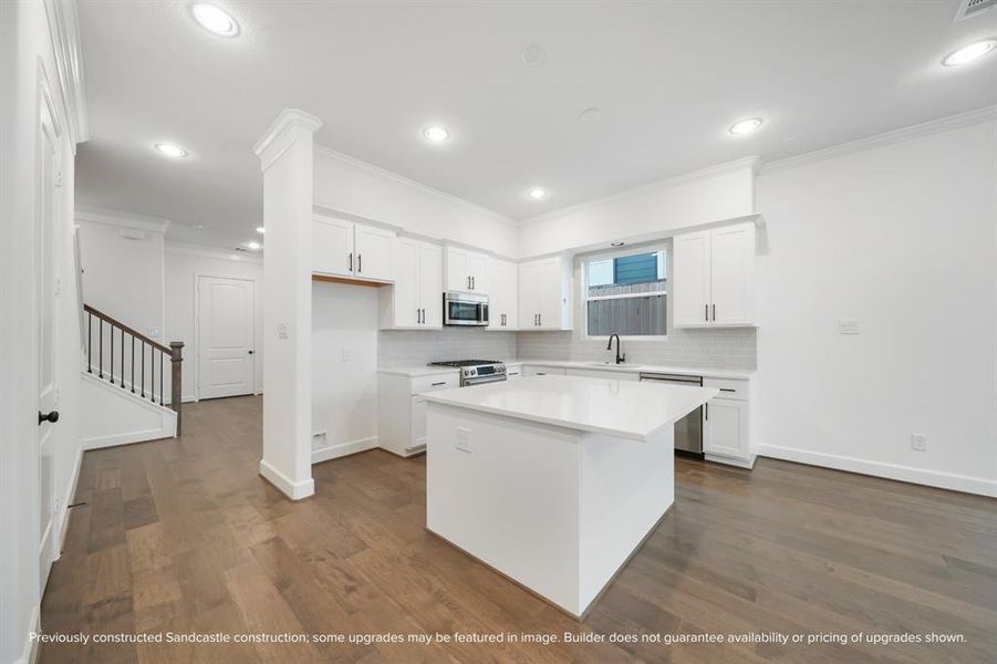 An alternate view unveils the kitchen’s grand island, serving as the heart of the home, with an inviting passage to the adjacent dining room, where memories await to be made.