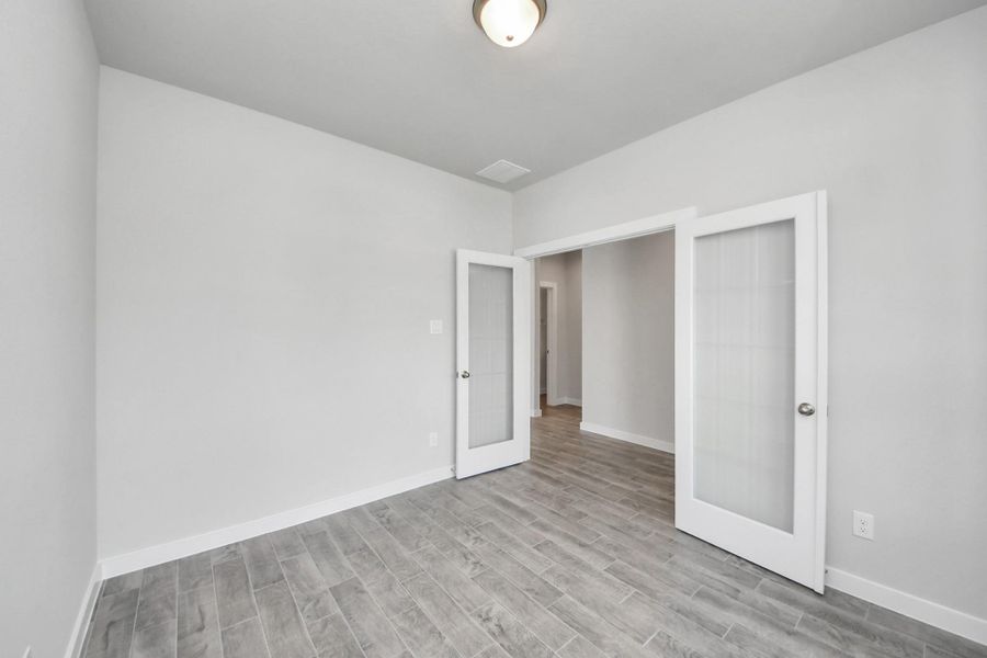 At the forefront, a refined home office beckons productivity and focus. Luxurious details like elegant wood-look tile flooring, custom paint, expansive windows with privacy blinds, and French doors create an inspiring workspace. Sample photo of completed home with similar floor plan. Actual colors and selections may vary.