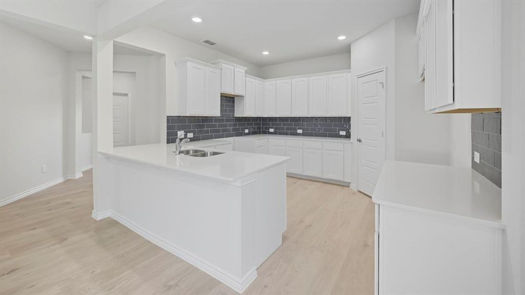 Kitchen with white cabinetry, tasteful backsplash, a peninsula, light stone countertops, and recessed lighting Kitchen with white cabinetry, tasteful backsplash, a peninsula, light stone countertops, and recessed lighting