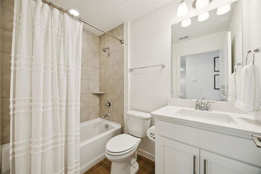 Secondary bathroom offers tub with shower and tile surround, tile flooring, vanity with quartz countertop and undermount wave sink.