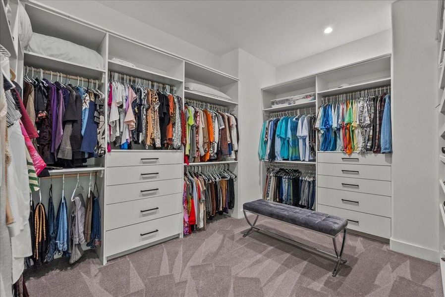 This expansive 14 x 11 primary walk-in closet features floor-to-ceiling custom built-ins, multiple drawer banks, and enough space for a center seating area.