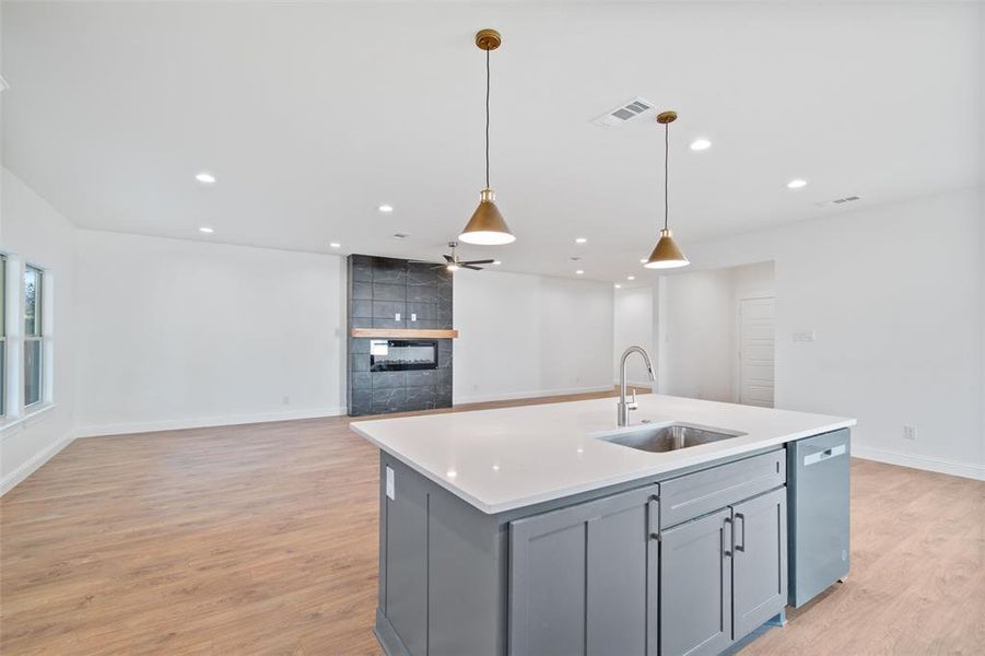 Kitchen featuring gray cabinetry, sink, stainless steel dishwasher, decorative light fixtures, and a kitchen island with sink