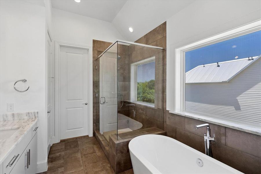 Contemporary bathroom featuring a freestanding soaking tub, a frameless glass shower enclosure, a dual-pane window, and a vanity with a light-colored countertop