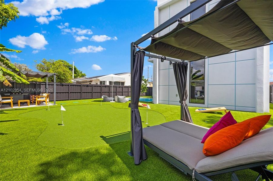 Backyard featuring a synthetic turf putting green, dark-toned privacy fencing, and a modern exterior facade with paneled cladding