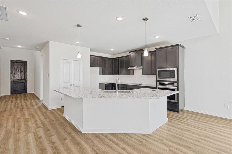 Kitchen with sink, light stone counters, a kitchen island with sink, dark brown cabinets, and appliances with stainless steel finishes