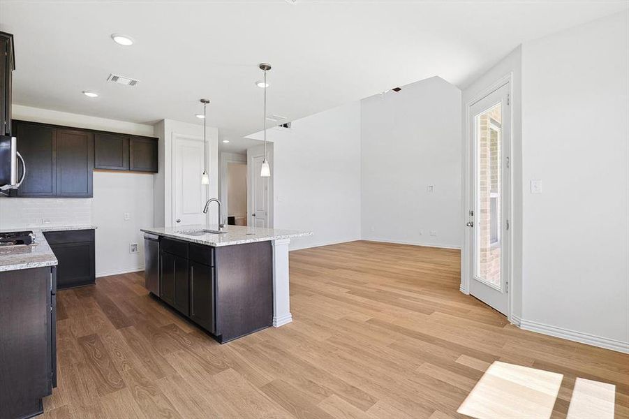 Kitchen featuring pendant lighting, light hardwood / wood-style flooring, stainless steel appliances, sink, and a center island with sink