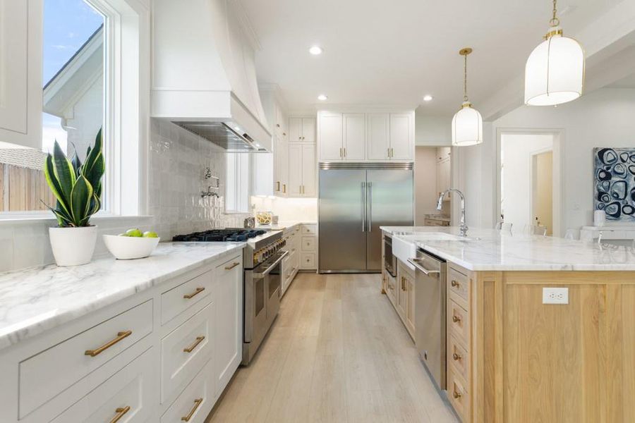 Kitchen featuring custom range hood, premium appliances, light stone countertops, hanging light fixtures, and backsplash