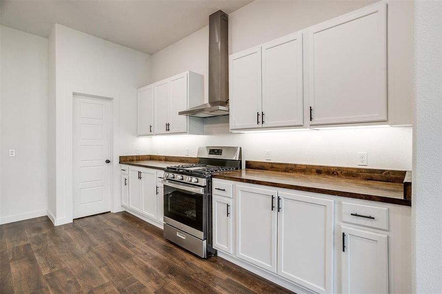 Kitchen with white cabinets, stainless steel gas range, wall chimney exhaust hood, and butcher block counters