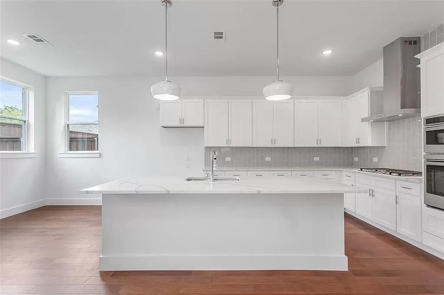 Kitchen with tasteful backsplash, a center island with sink, wall chimney range hood, and light stone countertops