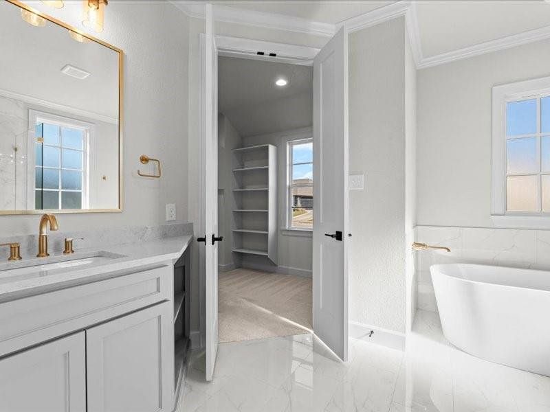 Bathroom featuring a freestanding tub, vanity, a walk in closet, light marble finish floors, and ornamental molding Bathroom featuring a freestanding tub, vanity, a walk in closet, light marble finish floors, and ornamental molding