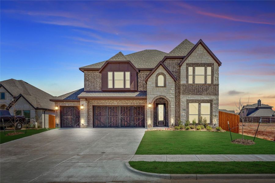 Two-story brick and stone home with three-car garage, arched entry, and manicured front lawn at dusk Two-story brick and stone home with three-car garage, arched entry, and manicured front lawn at dusk