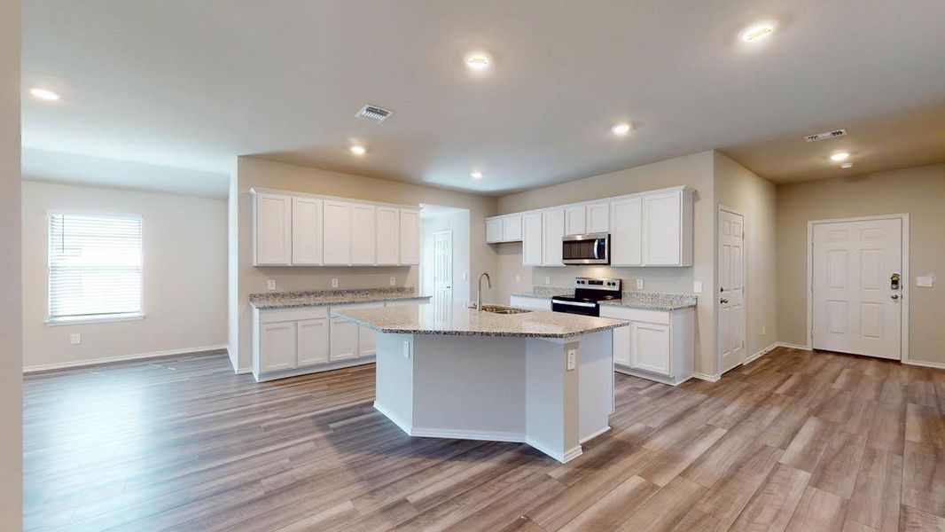 An open-concept kitchen and living area feature a spacious central island and wood-look flooring.