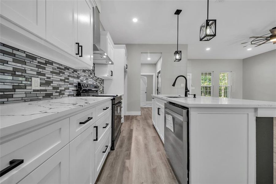 Kitchen featuring a center island with sink, black range with electric cooktop, hanging light fixtures, light wood-type flooring, and dishwasher