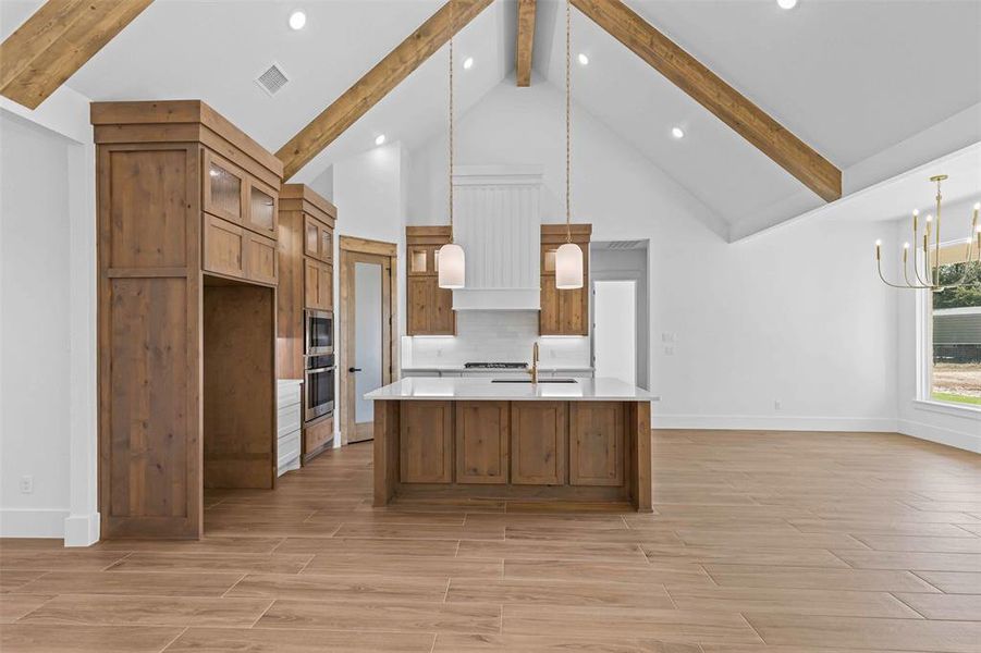 Kitchen featuring beam ceiling, brown cabinetry, pendant lighting, high vaulted ceiling, and backsplash