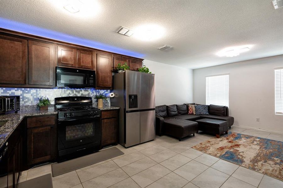 Kitchen featuring light tile patterned floors, black appliances, dark stone counters, and dark brown cabinetry