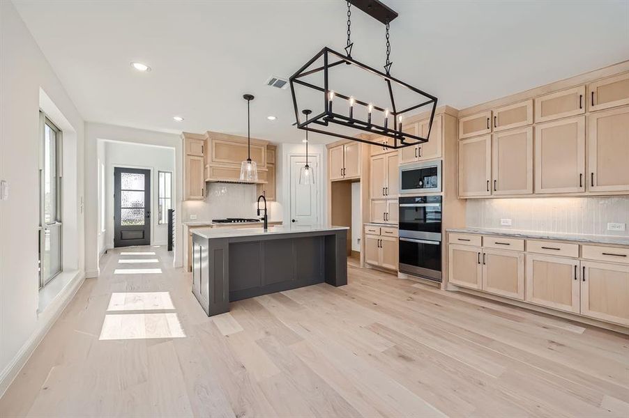 Kitchen featuring decorative backsplash, an island with sink, light hardwood / wood-style flooring, and hanging light fixtures